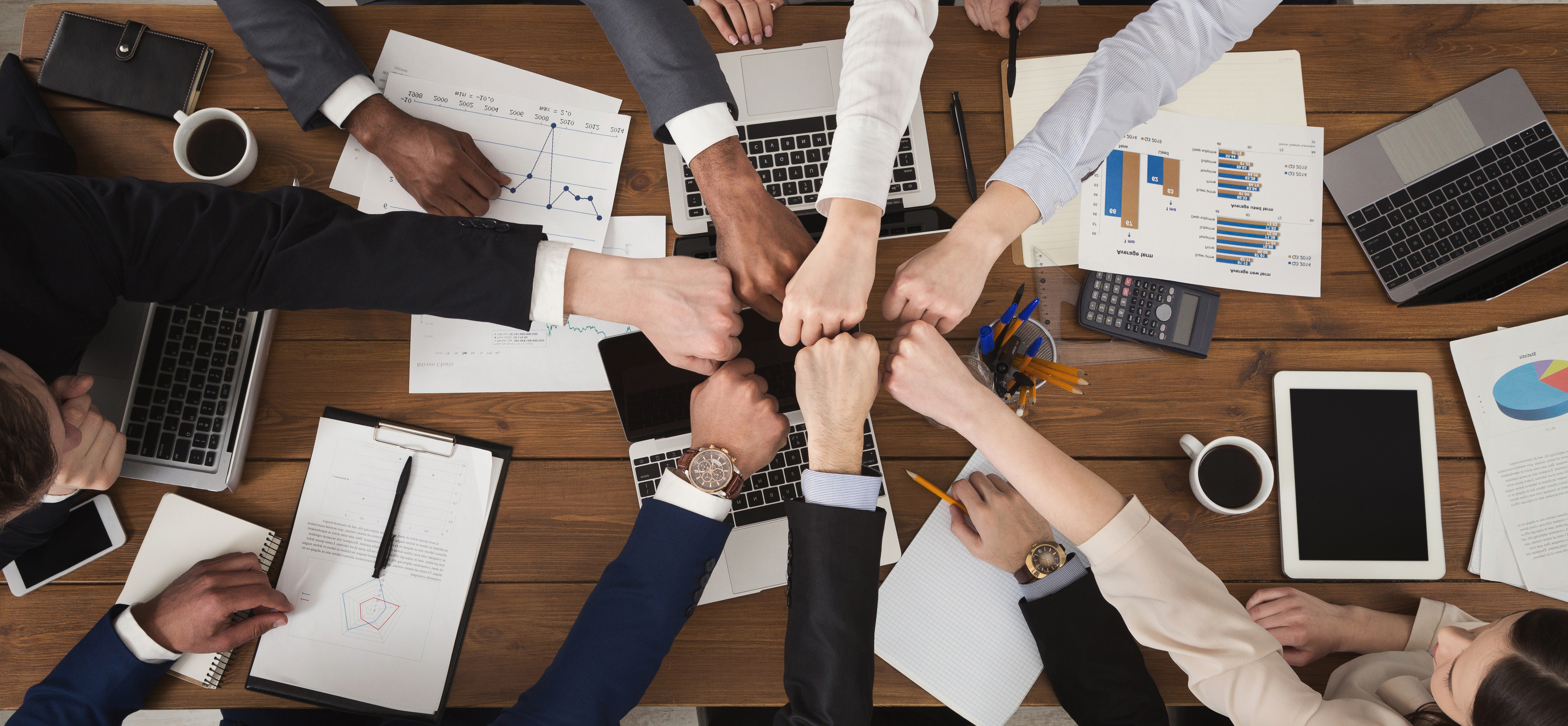 Young people putting their fists together as symbol of unity and achievement, top view. Group of people fist bump assemble together over workplace. Teamwork concept, copy space in middle